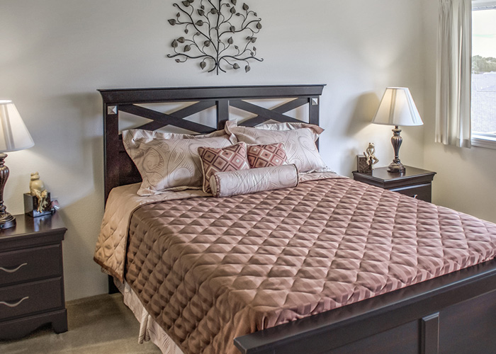 Well-decorated bedroom with a dark wood bed frame, beige and brown bedding, two bedside tables with lamps, and a window.