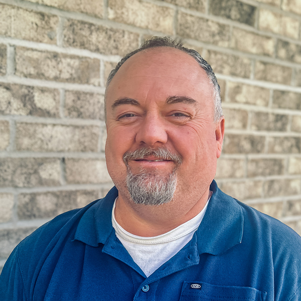 Bill Sager, Plant Operations Director at Mallard Point Senior Living, standing in front of a light brick wall and smiling while wearing a blue collared shirt.