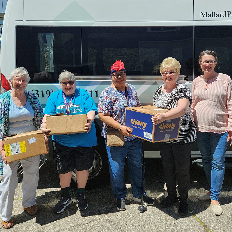 A group of residents and team members, some holding boxes, smiling in front of Mallard Point van.
