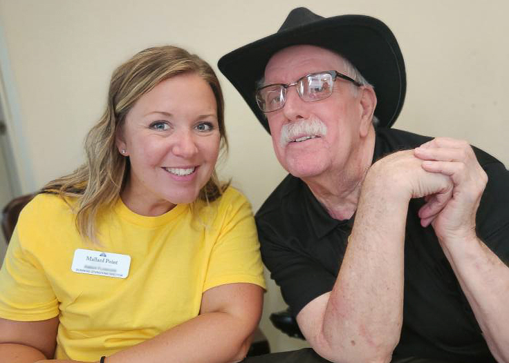 A young woman on the Mallard Point team smiles alongside a senior man in a black cowboy hat.