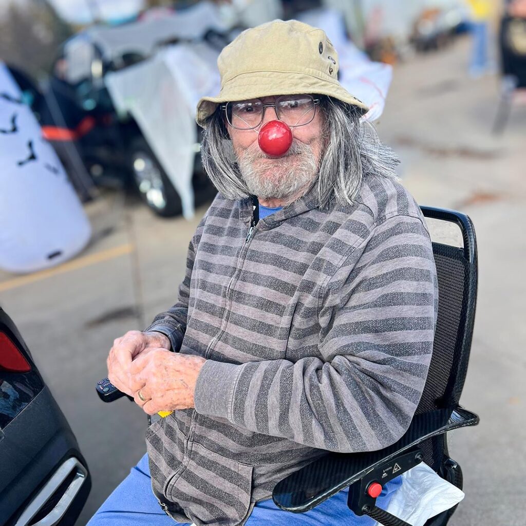 A senior man smiles at a local event wearing a red Rudolph nose.