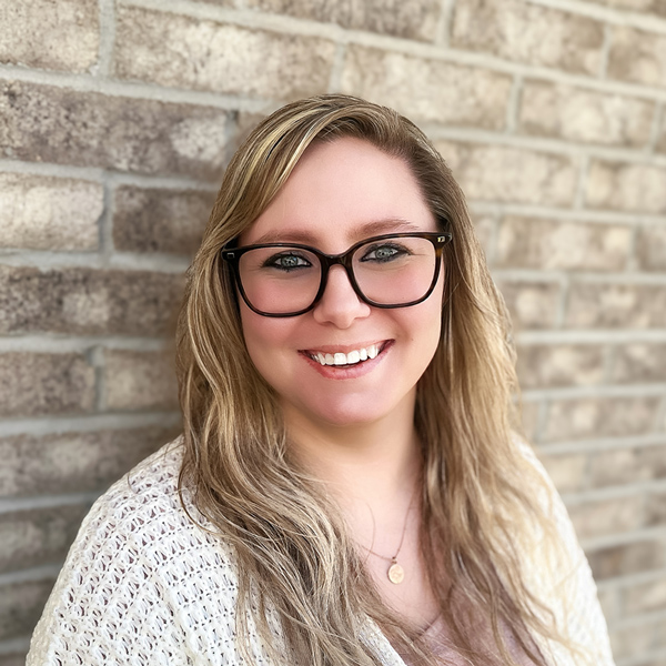 Michelle Rich, Resident Services Director at Mallard Point Senior Living, smiling in a professional headshot, wearing glasses and a light knit top, posed against a softly blurred brick wall background.