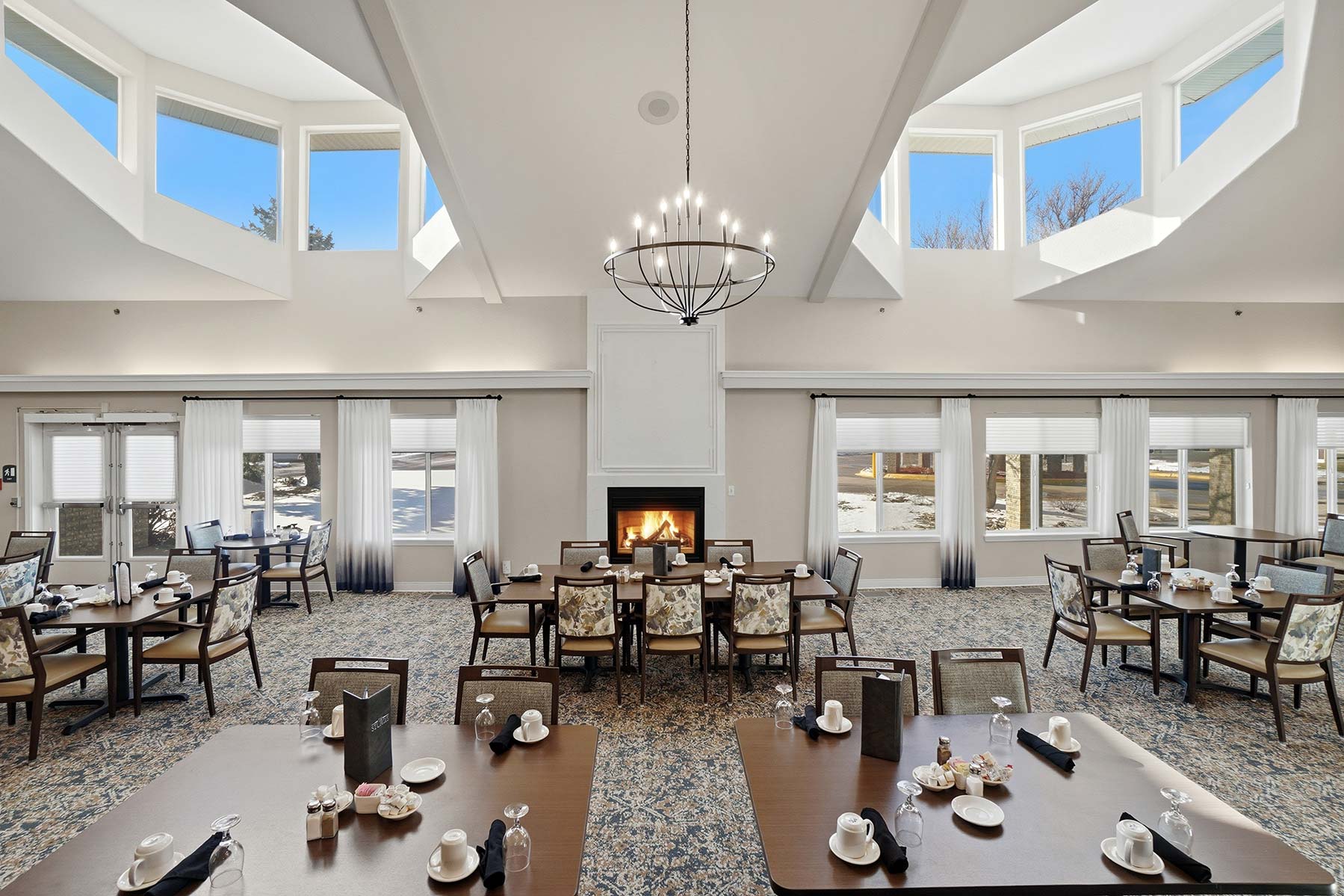 Spacious dining room at Mallard Point Senior Living with vaulted ceilings, skylight windows, chandelier, fireplace, and neatly set tables, renovation completed in 2025.