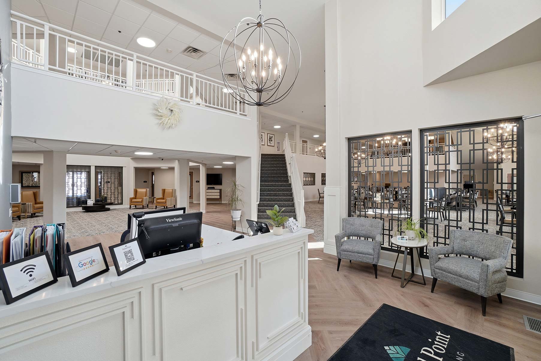 Front desk area showcasing elegant design, lighting, and view of staircase to upper level at Mallard Point Senior Living, renovation completed in 2025.