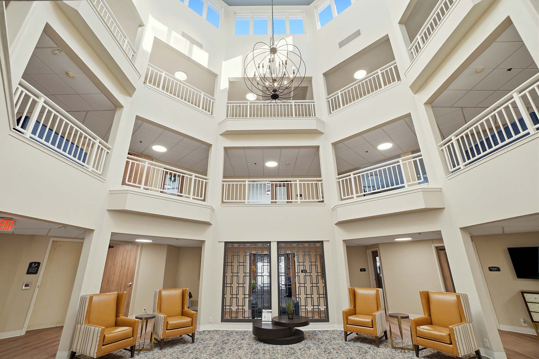 Three-story central atrium at Mallard Point Senior Living, decorated in cream shades with large hanging lighting fixture and high windows, renovation completed in 2025.