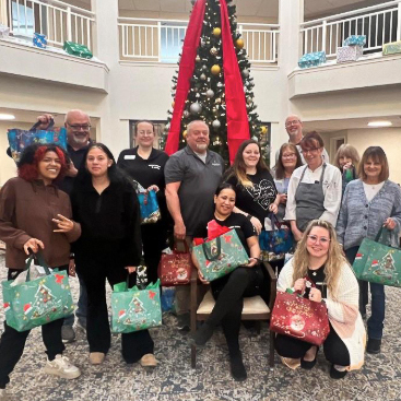The team at Mallard Point Senior Living smiles, holding Christmas gifts in festive surroundings.