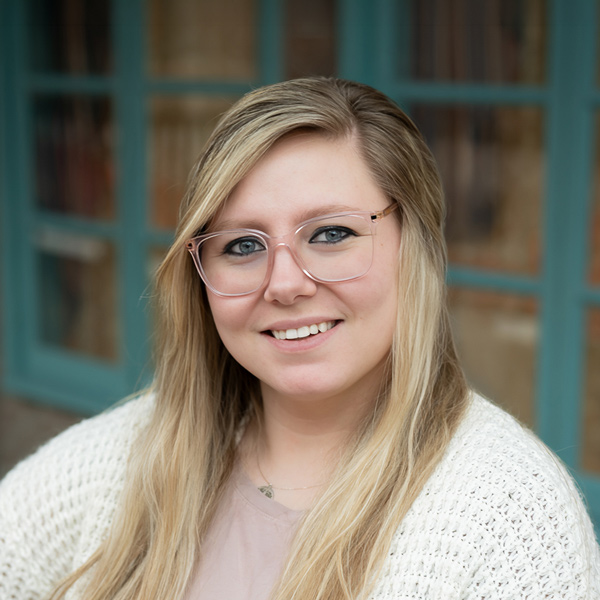Michelle Rich, Resident Services Director at Mallard Point Senior Living, smiling in a professional outdoor headshot with long blonde hair, pink glasses, a light knit cardigan, and softly blurred teal window details in the background.